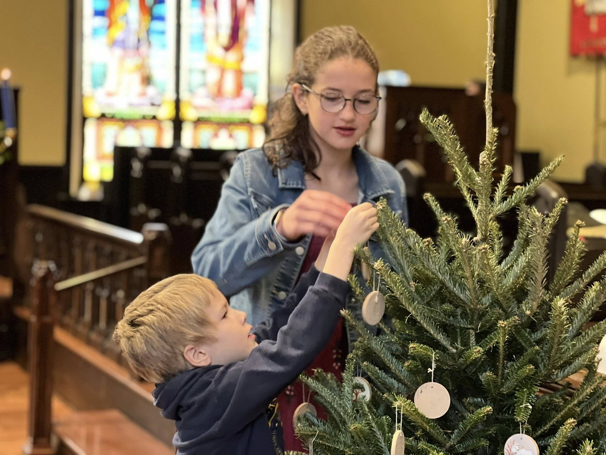 Children decorating a tree inside the church with stained glass in the background